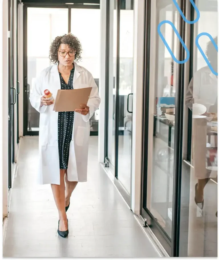 An image of a pharmacist walking down a hospital corridor holding a prescription and a folder.