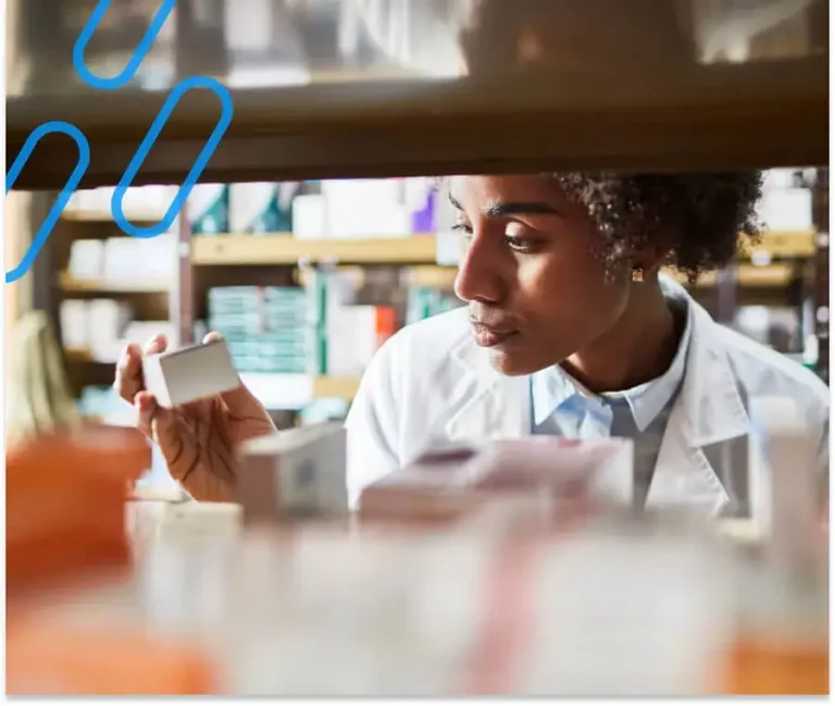 A pharmacist inspecting a prescription behind a bookshelf of many prescriptions.